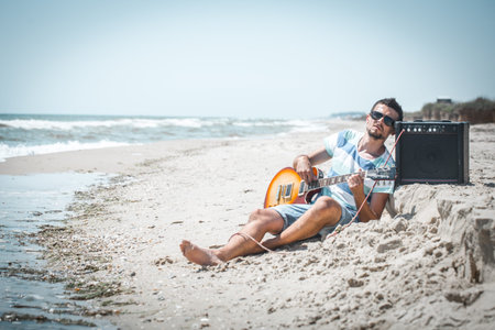 young stylish guy on the beach with musical instruments,the concept of music and relaxation