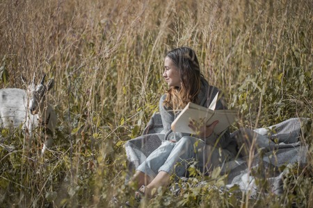 young girl on a field reading a bookの写真素材