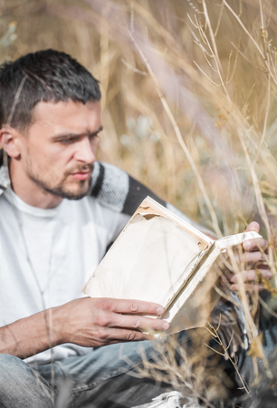 a young man on the field reading a bookの写真素材
