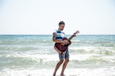 young man with acoustic guitar on the beach, joyful emotions, the concept of leisure and musicの写真素材