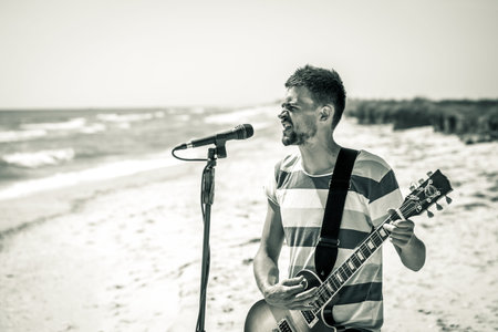 rock on the beach, the musician plays the guitar and sings into the microphone, the emotions of the musician, the concept of leisure and creativityの写真素材