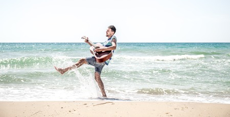 young man with acoustic guitar on the beach, joyful emotions, the concept of leisure and musicの写真素材