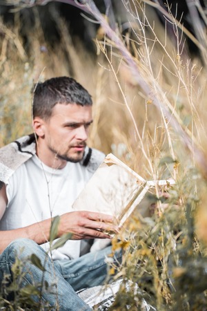 young handsome man on the field reading a book, the concept of rest and readingの写真素材