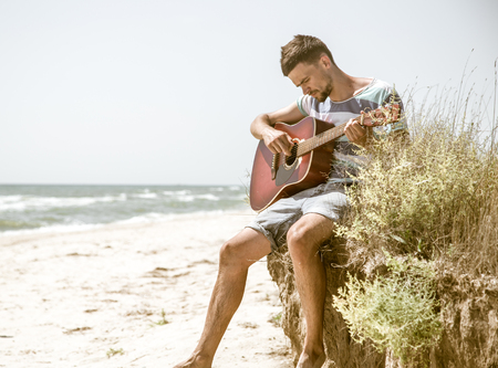 young man with acoustic guitar on the beach, the emotions of the musician, the concept of leisure and creativityの写真素材