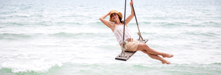 beautiful girl in a hat standing on the hanging swing on the sea on the beach of Thailandの写真素材