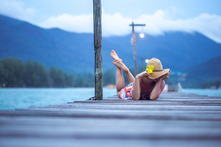 beautiful girl in a hat sitting on a long wooden pier in the evening on Koh Chang, Thailandの写真素材