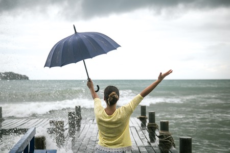 young girl on pier with umbrella stands with his back to the seaの写真素材