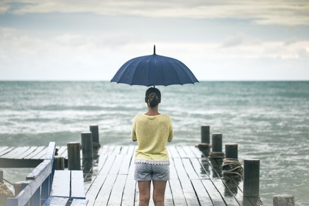 young girl on pier with umbrella stands with his back to the seaの写真素材