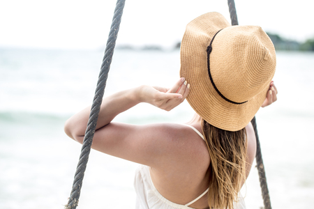 beautiful girl in a hat sitting on rocked back on the beach of Thailandの写真素材