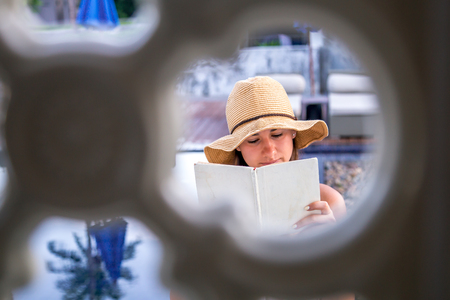 A young girl in a hat reading a book on holiday ,the concept of reading and relaxing , shooting through the lumenの写真素材