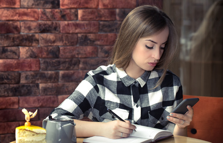 Beautiful girl sitting at the table in a cafe in a work process, concept of business and workの写真素材