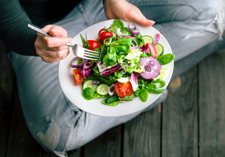 Fresh salad in the hands of the girl from above, the concept of healthy food and veggieの写真素材