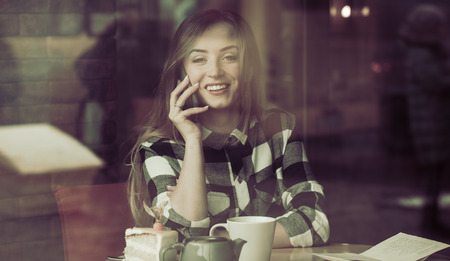 Beautiful girl with a phone in a cafe at the table, the concept of business and workの写真素材