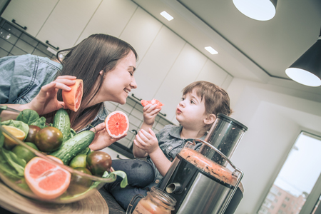 mother with two lovely daughters prepares fresh fruit juice in the kitchen, the concept of a healthy baby food and a happy familyの写真素材