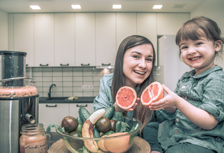 mother with two lovely daughters prepares fresh fruit juice in the kitchen, the concept of a healthy baby food and a happy familyの写真素材