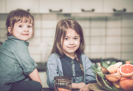 Two cute sisters sitting near a plate of fruit on the kitchen table, the concept of a healthy baby foodの写真素材
