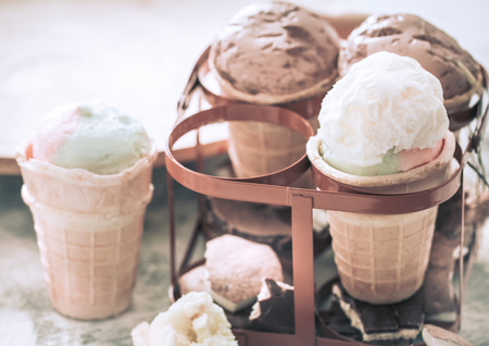 different ice cream in a cone stands in a beautiful stand on a wooden light background, a concept of summer sweets and ice creamの写真素材