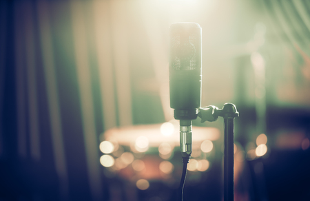 Microphone in recording Studio or concert hall close-up, with drum set on background out of focus. Beautiful blurred background of colored lanterns. Musical concept in vintage style.の写真素材