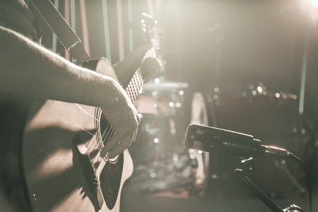 The Studio microphone records an acoustic guitar close-up, in a recording Studio or concert hall, with a drum set on a background in out-of-focus mode. Beautiful blurred background of colored lanterns. Musical concept in vintage style.の写真素材