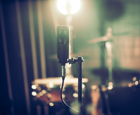 Microphone in recording Studio or concert hall close-up, with drum set on background out of focus. Beautiful blurred background of colored lanterns. Musical concept in vintage style.の写真素材