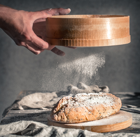 baker with flour in his hand and fresh bread on a beautiful wooden background, the concept of healthy food and bakery industryの写真素材