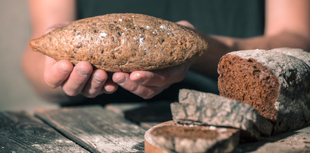 baker holding fresh bread in hands on a beautiful wooden background, concept of healthy eating and baking industryの写真素材