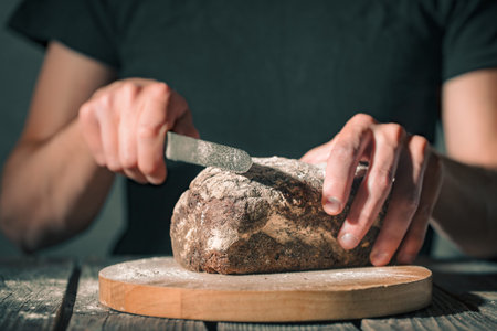 baker cuts fresh bread on a beautiful wooden background, the concept of healthy food and bakery...