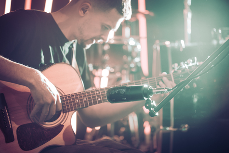 The Studio microphone records an acoustic guitar close-up, in a recording Studio or concert hall, with a drum set on a background in out-of-focus mode. Beautiful blurred background of colored lanternsの写真素材