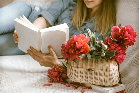 Girl on the couch with red peonies reading a bookの写真素材