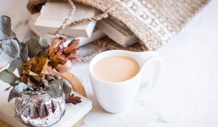 still life on a light wooden background, vase with flowers and books with a cup of coffee, interior...