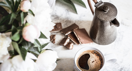 Still life with a cup of coffee and fresh peony flowers on a light wooden backgroundの写真素材