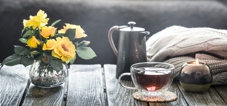 cup of tea with a teapot and roses in a vase, stand in the living room at home on a wooden tableの写真素材