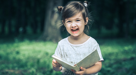 little cute little girl is reading a book in the park on a background of green natureの写真素材
