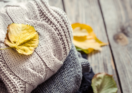 a stack of knitted cozy sweaters and autumn leaves on a wooden backgroundの写真素材