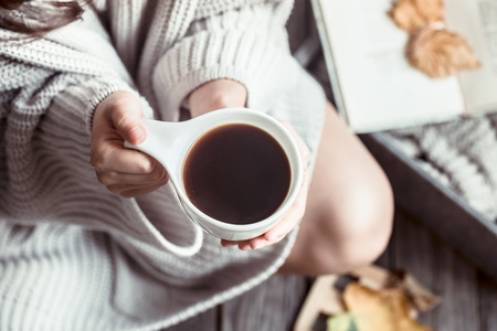 Girl with a cup of coffee in hands on a wooden background, the concept of home comfort and cozinessの写真素材