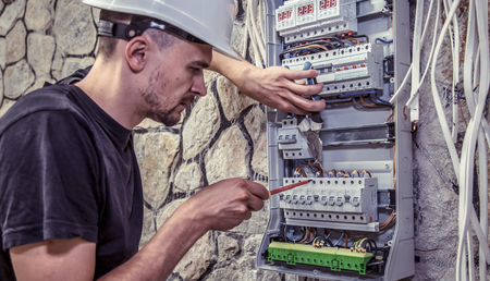 a male electrician works in a switchboard with an electrical connecting cable, connects the equipment with tools, the concept of complex work, space for textの写真素材