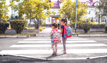 Children go to school, happy students with school backpacks and holding hands together, cross the road, the concept of education with girls, space for textの写真素材