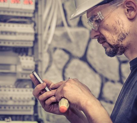 a male electrician works in a switchboard with an electrical connecting cable, connects the equipment with tools, the concept of complex work, space for textの写真素材