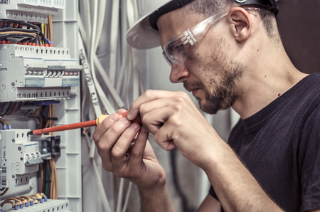a male electrician works in a switchboard with an electrical connecting cable, connects the equipment with tools, the concept of complex work, space for textの写真素材