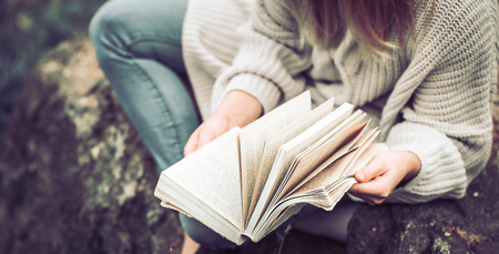 Young girl in a warm sweater reads a book on nature view from above, concept of leisure and hobbyの写真素材