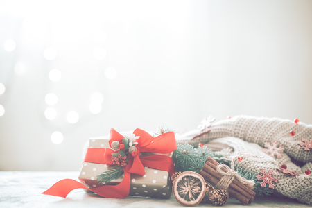Christmas coziness in a room on a light background, with lights and branches of a Christmas tree and a gift with a red bow on the table, space for textの写真素材