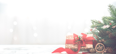 Christmas coziness in a room on a light background, with lights and branches of a Christmas tree and a gift with a red bow on the table, space for textの写真素材
