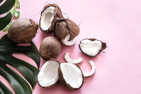 Fresh coconut halves and tropical leaves on a pink background, pop art. Top view, close-up, creative conceptの写真素材