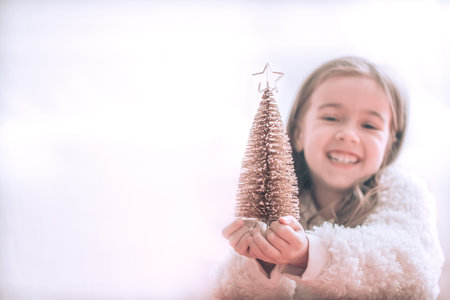 Christmas background with a cute little girl and a beautiful little tree in the hands of a girl on a...