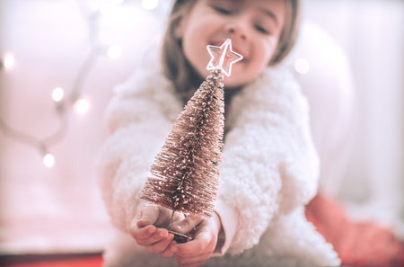 Christmas background with a cute little girl and a beautiful little tree in the hands of a girl on a...