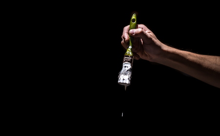 male hand holding a brush with white paint on a black background. Man in industrial concept. there is a place for text, object close upの写真素材