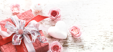 Valentine's day and mother's day concept, red gift box with bow and roses on light wooden backgroundの写真素材