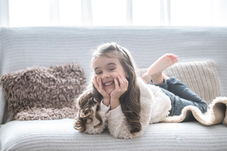 happy little girl lying on the couch, beautiful smile, rest conceptの写真素材