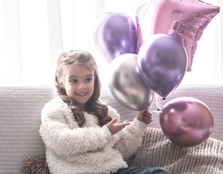 little girl with balloons sitting on the couch, holiday conceptの写真素材