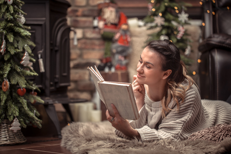 girl reading a book in a cozy home atmosphere near the fireplace, the concept of home restの写真素材